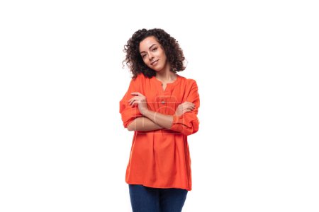 Téléchargez les photos : Jeune dame brune bouclée vêtue d'un élégant chemisier orange vif sur un fond blanc avec espace de copie. - en image libre de droit