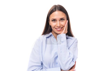 Téléchargez les photos : Portrait d'une jeune femme modèle caucasienne au maquillage clair et aux cheveux raides foncés vêtus d'un chemisier bleu sur fond blanc avec espace de copie. - en image libre de droit