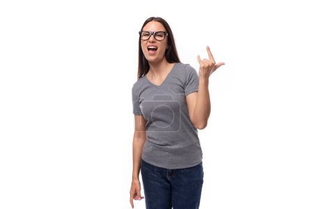 Téléchargez les photos : Jeune jolie femme brune dans un t-shirt gris et des lunettes sur un fond blanc avec espace de copie. - en image libre de droit