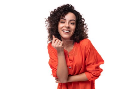 Téléchargez les photos : Jeune femme caucasienne positive énergique aux cheveux bouclés noirs est habillé d'une chemise orange sur un fond blanc. - en image libre de droit