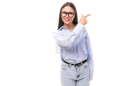 Téléchargez les photos : Jolie jeune femme brune européenne vêtue d'une chemise bleue pointe les mains vers un objet sur un fond isolé avec espace de copie. - en image libre de droit