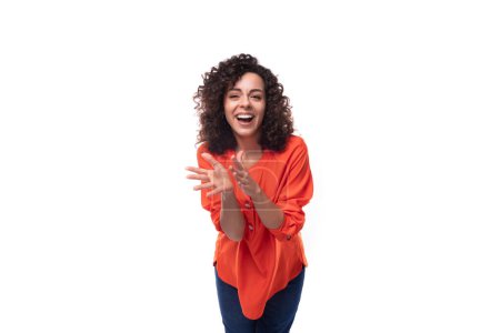 Téléchargez les photos : Jeune femme brune caucasienne aux cheveux bouclés habillé en chemisier orange souriant sur fond blanc avec espace de copie. - en image libre de droit