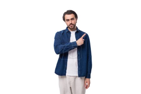 Téléchargez les photos : Jeune homme caucasien élégant intelligent aux cheveux noirs habillé d'une chemise bleue est inspiré par une idée et montre son index sur un fond blanc. - en image libre de droit