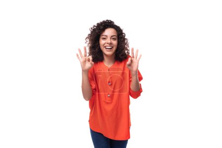Foto de Joven caucásico morena mujer con pelo rizado vestido de naranja blusa sonriendo sobre fondo blanco con espacio de copia. - Imagen libre de derechos