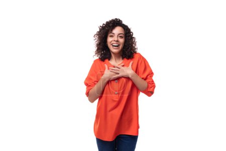 Téléchargez les photos : Jeune femme brune bouclée vêtue d'un chemisier orange sur fond blanc. - en image libre de droit