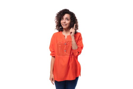 Téléchargez les photos : Jeune femme brune bouclée vêtue d'un chemisier orange parle au téléphone. - en image libre de droit