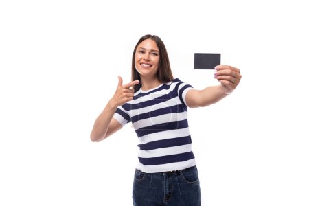 Téléchargez les photos : Jeune femme brune bien soignée aux cheveux raides vêtue d'un t-shirt rayé tenant un smartphone avec une maquette. - en image libre de droit