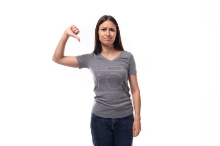 Téléchargez les photos : Jeune femme brune positive montre un t-shirt avec espace pour imprimer des identités sur un fond blanc avec espace de copie. - en image libre de droit