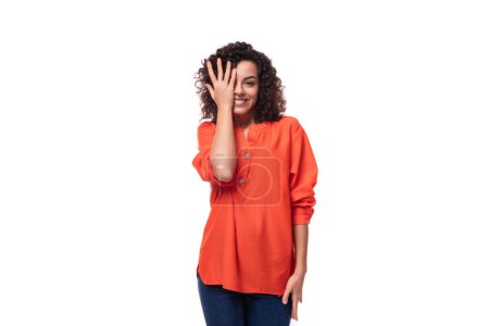 Téléchargez les photos : Jeune femme brune bouclée vêtue d'un chemisier orange sur fond blanc. - en image libre de droit