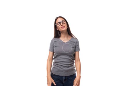 Foto de Joven morena positiva con gafas se viste con una camiseta gris con una maqueta para imprimir sobre un fondo blanco con espacio para copiar. - Imagen libre de derechos