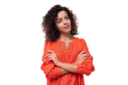Foto de Joven exitosa mujer europea con el pelo negro rizado se mantiene vestida con una blusa naranja brillante. - Imagen libre de derechos