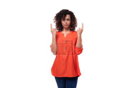 Téléchargez les photos : Jeune femme européenne sérieuse avec les cheveux noirs bouclés dans une chemise orange tient ses mains vers le haut. - en image libre de droit