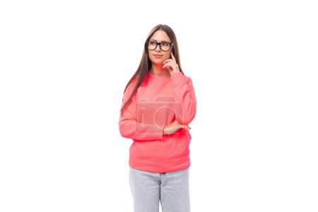 Téléchargez les photos : Belle jeune femme brune européenne bien entretenue en lunettes vêtue d'un sweat-shirt rose sur un fond blanc isolé avec espace de copie. - en image libre de droit