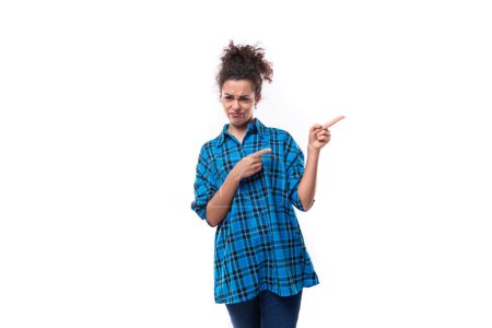 Téléchargez les photos : Jeune femme européenne aux cheveux foncés vêtue de façon informelle d'un chemisier à carreaux bleu avec sa main sur le côté isolé sur fond blanc. - en image libre de droit