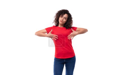 Foto de Caucásico joven lindo rizado morena mujer mostrando espacio en rojo camiseta. - Imagen libre de derechos