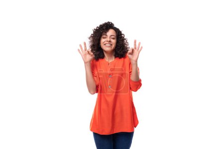 Téléchargez les photos : Jeune femme caucasienne positive énergique aux cheveux bouclés noirs est habillé d'une chemise orange sur un fond blanc. - en image libre de droit