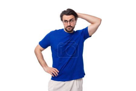 Téléchargez les photos : Portrait d'un jeune homme brune avec une barbe bien soignée vêtue d'un t-shirt bleu sur fond blanc avec espace de copie. - en image libre de droit