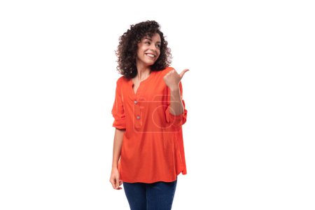 Téléchargez les photos : Jeune femme brune caucasienne aux cheveux bouclés habillé en chemisier orange souriant sur fond blanc avec espace de copie. - en image libre de droit