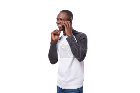 Téléchargez les photos : Jeune Américain avec une coupe de cheveux courte portant un pull à manches longues riant tout en parlant au téléphone. - en image libre de droit