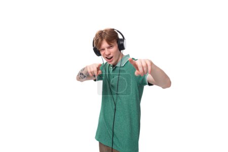 Foto de Joven positivo esbelto estudiante europeo hombre con pelo rojo escucha música en los auriculares con un cable. - Imagen libre de derechos