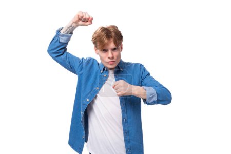 Foto de Joven fuerte confiado europeo chico con el pelo dorado vestido con una camisa de mezclilla azul sobre un fondo blanco. - Imagen libre de derechos