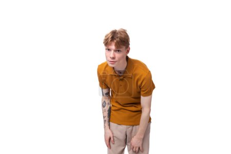 Téléchargez les photos : Jeune homme aux cheveux roux élégant avec une coupe de cheveux et un tatouage sur le bras est habillé d'un t-shirt jaune. - en image libre de droit