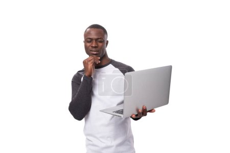 Foto de Un joven americano vestido con un suéter de manga larga posee un portátil para el trabajo remoto. - Imagen libre de derechos