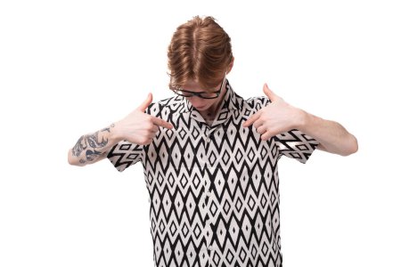 a young red-haired guy in glasses dressed in a summer shirt shows his hand down to the advertising space.