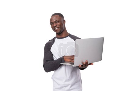 Foto de Un joven americano vestido con un suéter de manga larga sostiene un portátil para trabajar en sus manos. - Imagen libre de derechos