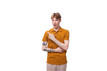 Téléchargez les photos : Jeune homme roux avec une coupe de cheveux courte et un tatouage sur le bras est habillé d'un t-shirt jaune. - en image libre de droit