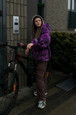 Nice young woman standing near the house with a bicycle.