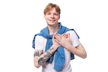 Téléchargez les photos : Portrait d'un jeune homme européen élégant à la mode aux cheveux roux et un tatouage sur les bras sur un fond de studio. concept de style de vie. - en image libre de droit