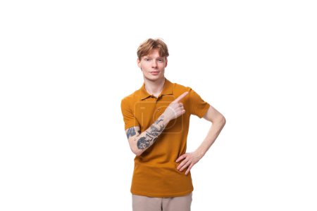 junger schlanker kaukasischer Mann mit roten kurzen Haaren und Tätowierung auf dem Arm trägt ein gelbes T-Shirt.