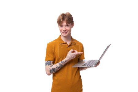 ein junger Mann mit kurzen roten Haaren in einem Sommer-T-Shirt benutzt einen Laptop.