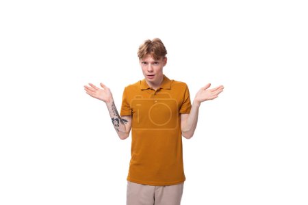 Téléchargez les photos : Jeune homme roux avec une coupe de cheveux courte et un tatouage sur le bras est habillé d'un t-shirt jaune. - en image libre de droit