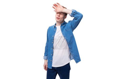 Foto de Joven europeo hombre con el pelo rojo lleva una camisa de mezclilla azul piensa en una idea. - Imagen libre de derechos