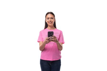 Foto de Joven mujer morena delgada en una camiseta básica rosa charlando por teléfono sobre un fondo blanco con espacio para copiar. - Imagen libre de derechos