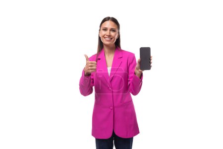 junge fröhliche positive Büroangestellte mit schwarzen Haaren in fliederfarbener Jacke demonstriert ein Smartphone mit einer Werbeattrappe.