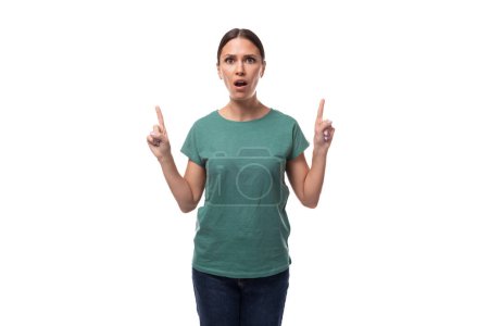 jeune femme aux cheveux noirs positive joyeuse dans un t-shirt de base vert rapporte les nouvelles sur un fond blanc avec espace de copie.