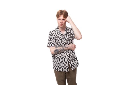 Foto de Un joven indigno con el pelo rojo y un tatuaje en los brazos está vestido con una camisa de manga corta que experimenta emociones negativas. - Imagen libre de derechos