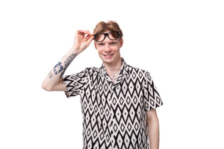 un joven caucásico con el pelo rojo vestido con una camisa tiene mala vista y lleva gafas.