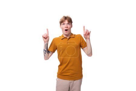 Téléchargez les photos : Jeune homme roux joyeux avec une coupe de cheveux et un tatouage sur son bras est habillé d'un t-shirt jaune d'été. - en image libre de droit
