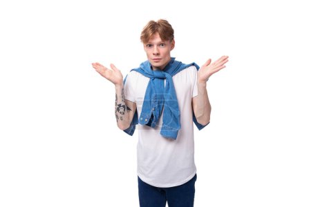 Foto de Joven hombre europeo pensativo con el pelo rojo y un tatuaje en sus brazos en una camiseta blanca es lluvia de ideas sobre un fondo blanco con espacio para copiar. - Imagen libre de derechos