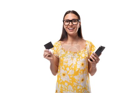Femme européenne avec des danses de cheveux noirs fluides droites tenant une carte de salaire en plastique et un smartphone dans ses mains.