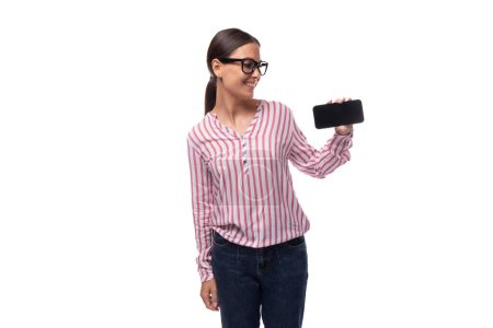 jeune employée de bureau habillée en chemisier rose blanc et jeans montre écran smartphone avec maquette.