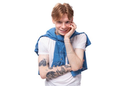 Foto de Retrato de un joven europeo pensativo con el pelo rojo y un tatuaje en los brazos sobre un fondo de estudio. concepto de estilo de vida. - Imagen libre de derechos