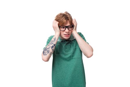 young smart caucasian man with red hair dressed in a green t-shirt is worried holding his head.
