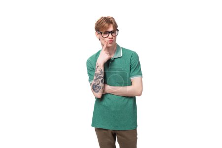 junger heller Mann mit Tätowierung auf dem Arm, bekleidet mit einem grünen Kurzarm-T-Shirt, das auf weißem Hintergrund posiert.