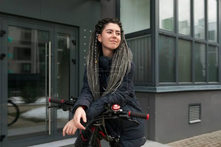 Cute young woman with dreadlocks riding a bicycle in the city.
