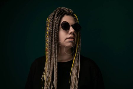 Eine Frau mit langen Dreadlocks steht in einem schwarzen Hemd. Ihre Haare sind aufwendig zu Dreadlocks gestylt, die sich über ihren Rücken ergießen. Sie strahlt Vertrauen und Individualität durch ihre einzigartige